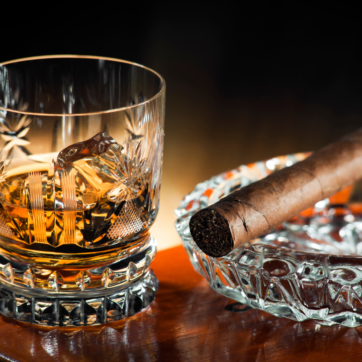 Glass of premium whiskey with ice beside a high-end cigar resting in a crystal ashtray